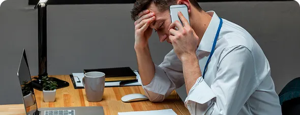 Directivo preocupado, con la mano en la frente, hablando por teléfono junto a su portátil