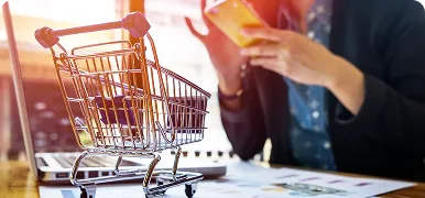Carrito de la compra junto a un portátil y una persona con una tarjeta de pago